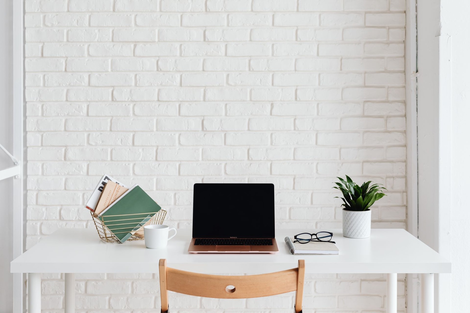 Bright, organized desk with a laptop, green folders, glasses, and a plant