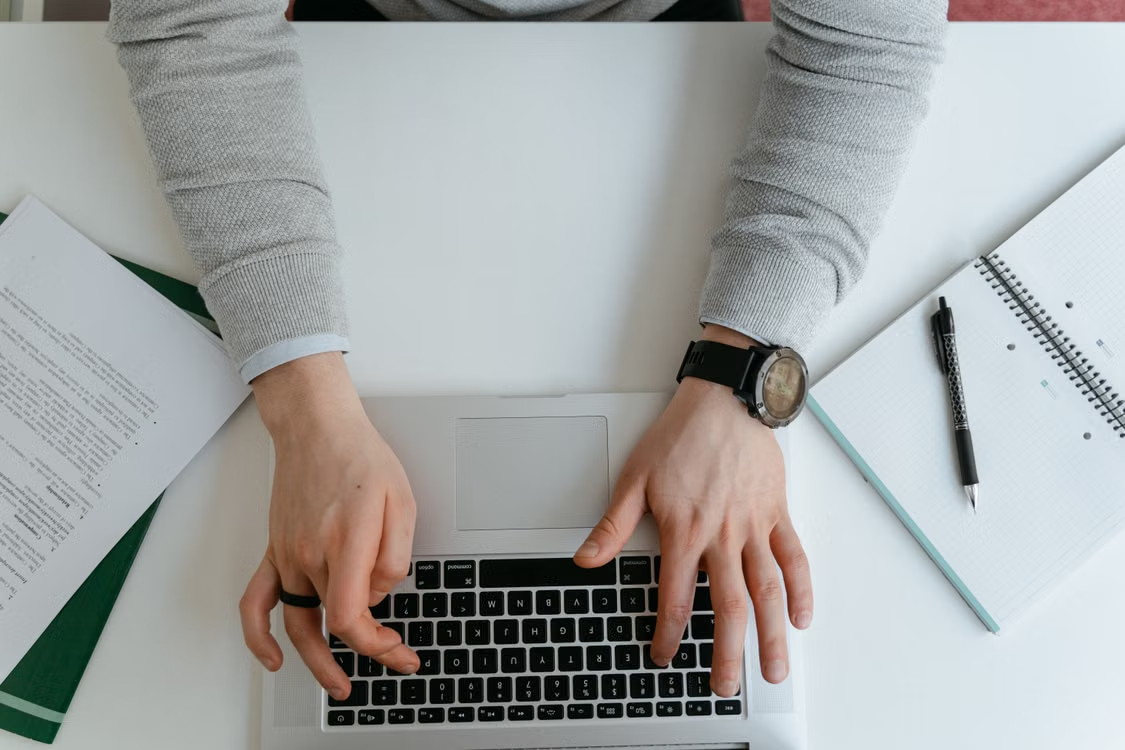 Overhead view of hands typing on a laptop beside work documents and a notebook